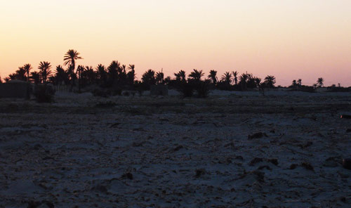 sunset by Tiboda village by the beach, showing a few mud houses and palm trees