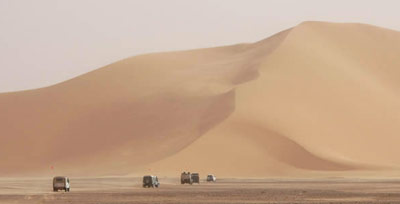 Sand mountains approached by a convoy of desert vehicles.